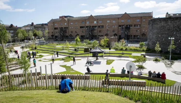 A widely shot image of a sunny communal square with much greenery around.