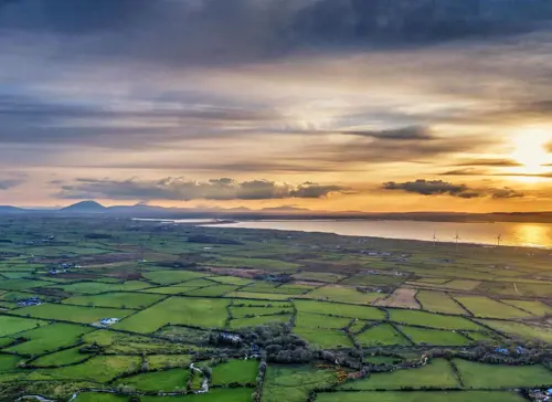 Green Irish landscape with sun rising in the clouds.