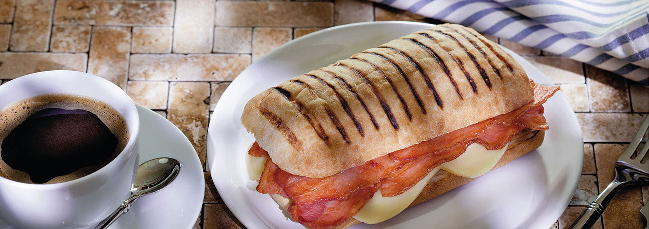 Panini sandwich on plate, on table beside a cup of coffee